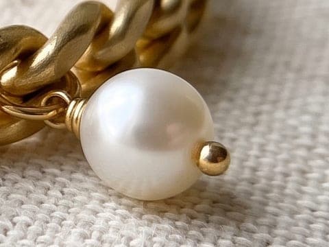 Close detail of the pearl charm and chain links, crisp with visible linen weave