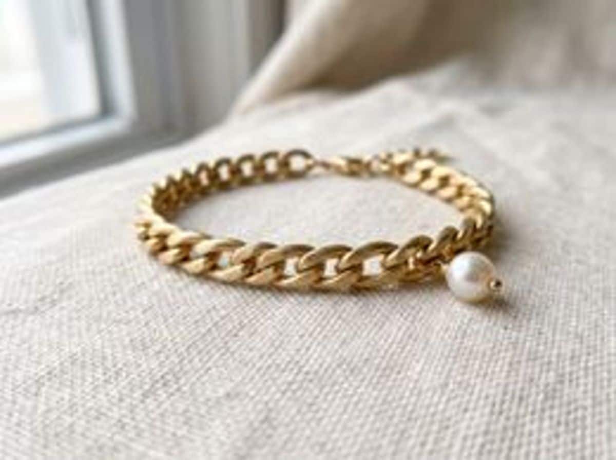 A gold chain bracelet with a pearl charm on linen, soft and low-detail from a small phone crop