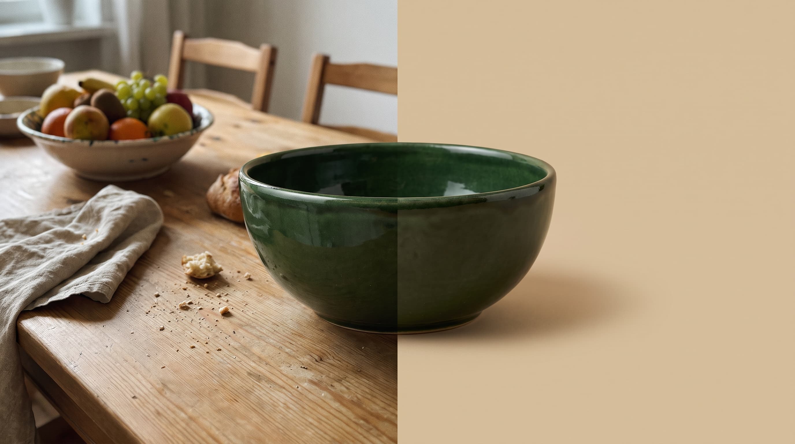 A dark forest green glazed ceramic bowl on a busy kitchen table with a fruit bowl and linen napkin on the left, cut out onto a flat sand beige background on the right