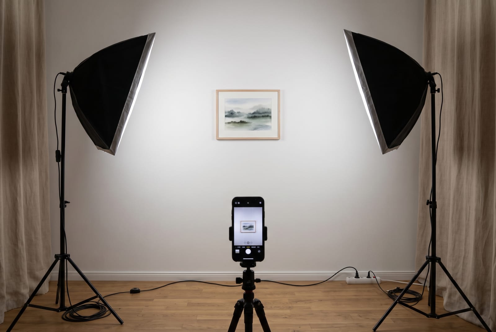 A setup view with a small painting on a wall, a light on each side at about 45 degrees, and a phone on a tripod centered in front