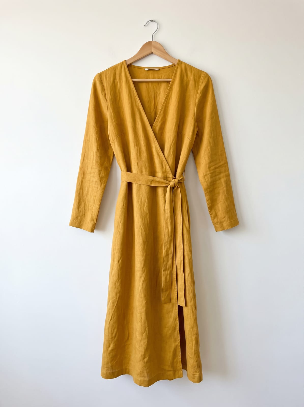 A mustard-yellow wrap dress on a wooden hanger against a white wall, centered in a portrait frame